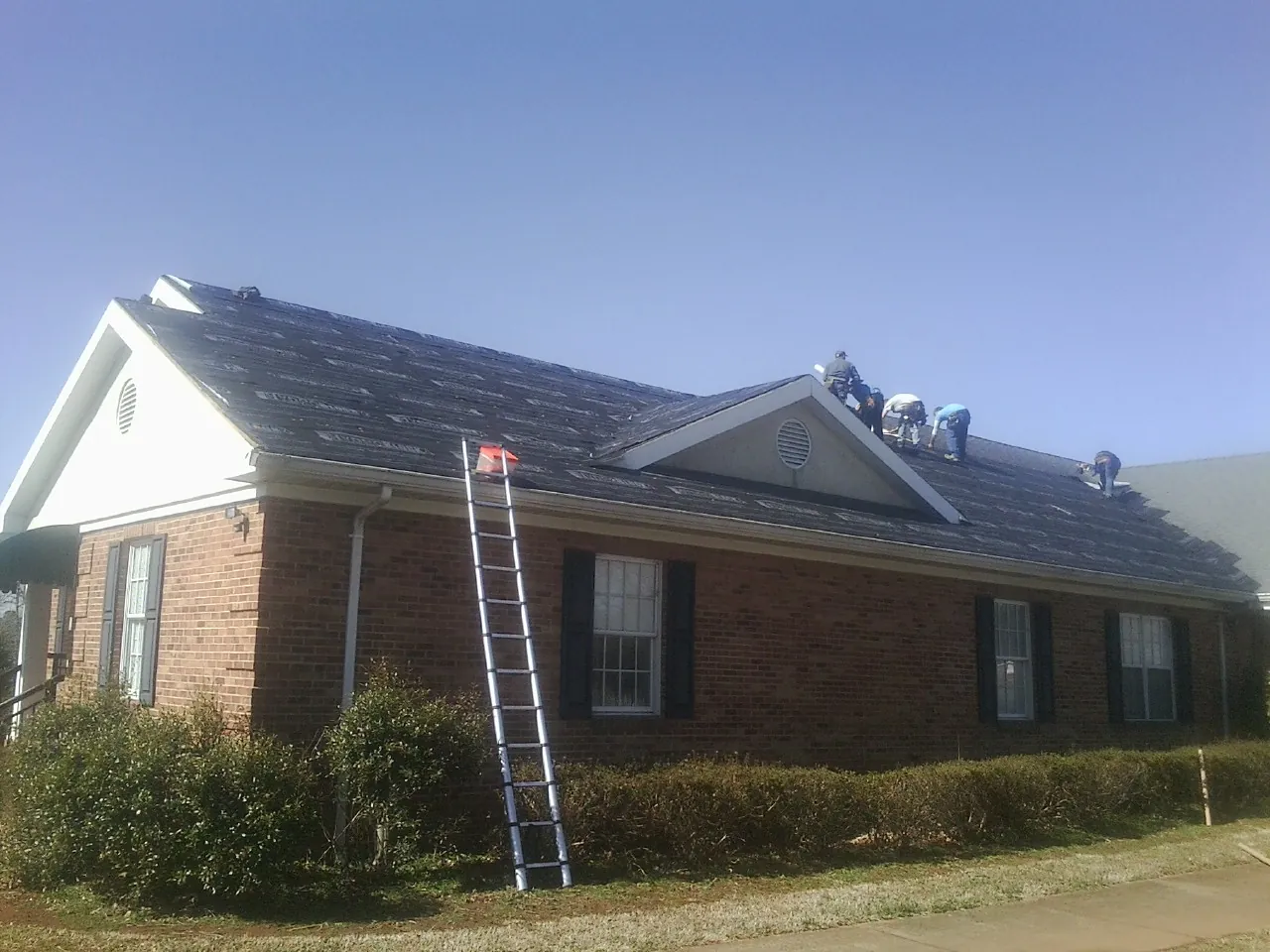 Crew tearing shingles off a brick ranch roof with a ladder set — Metal Roof Repair work by our crew in Maysville